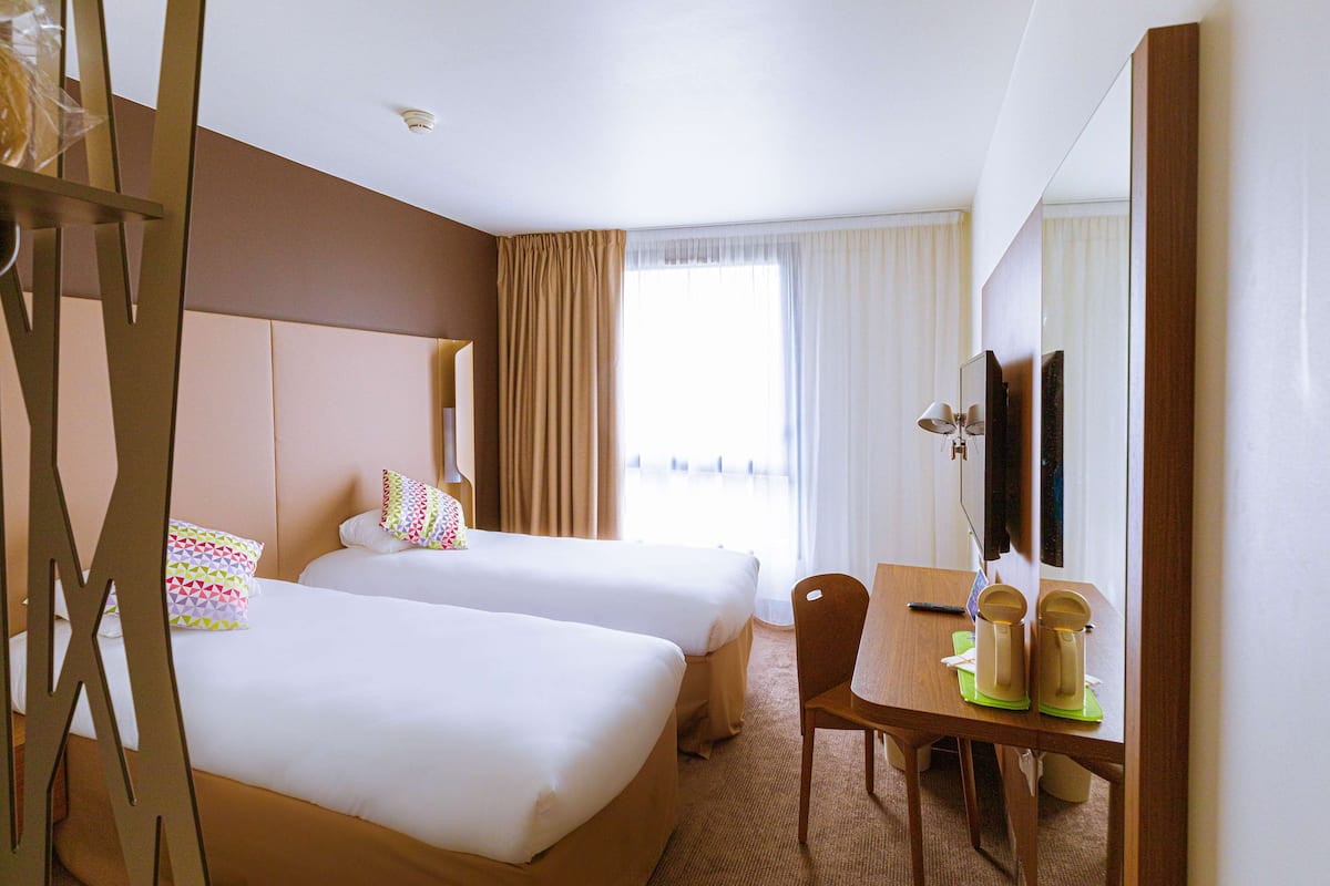 Habitación de hotel con dos camas, un escritorio, una silla y un televisor.