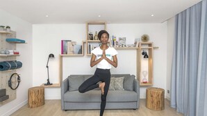 A person performing a yoga pose in a living room with a grey sofa, wooden shelves, and a yoga mat. - Campanile PRIME - Rungis Orly (Chevilly-Larue)