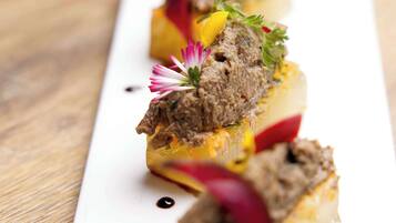 A white rectangular plate with three meat-based appetizers, each garnished with a flower and a slice of red vegetable, on a wooden table.