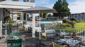 An outdoor dining area with tables and chairs, umbrellas, and a view of a building with a mural. - Campanile PRIME - Rungis Orly (Chevilly-Larue)