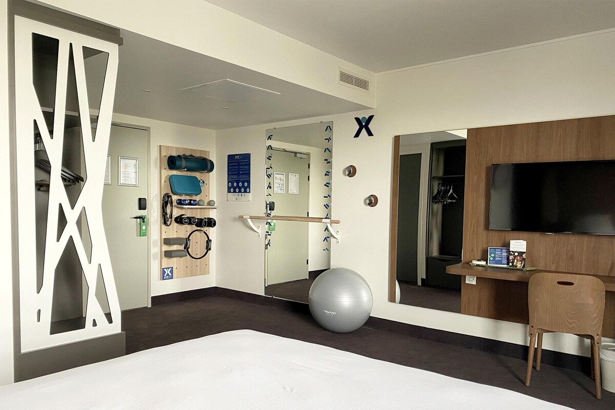 A hotel room with a bed, exercise equipment, a TV, and a desk.