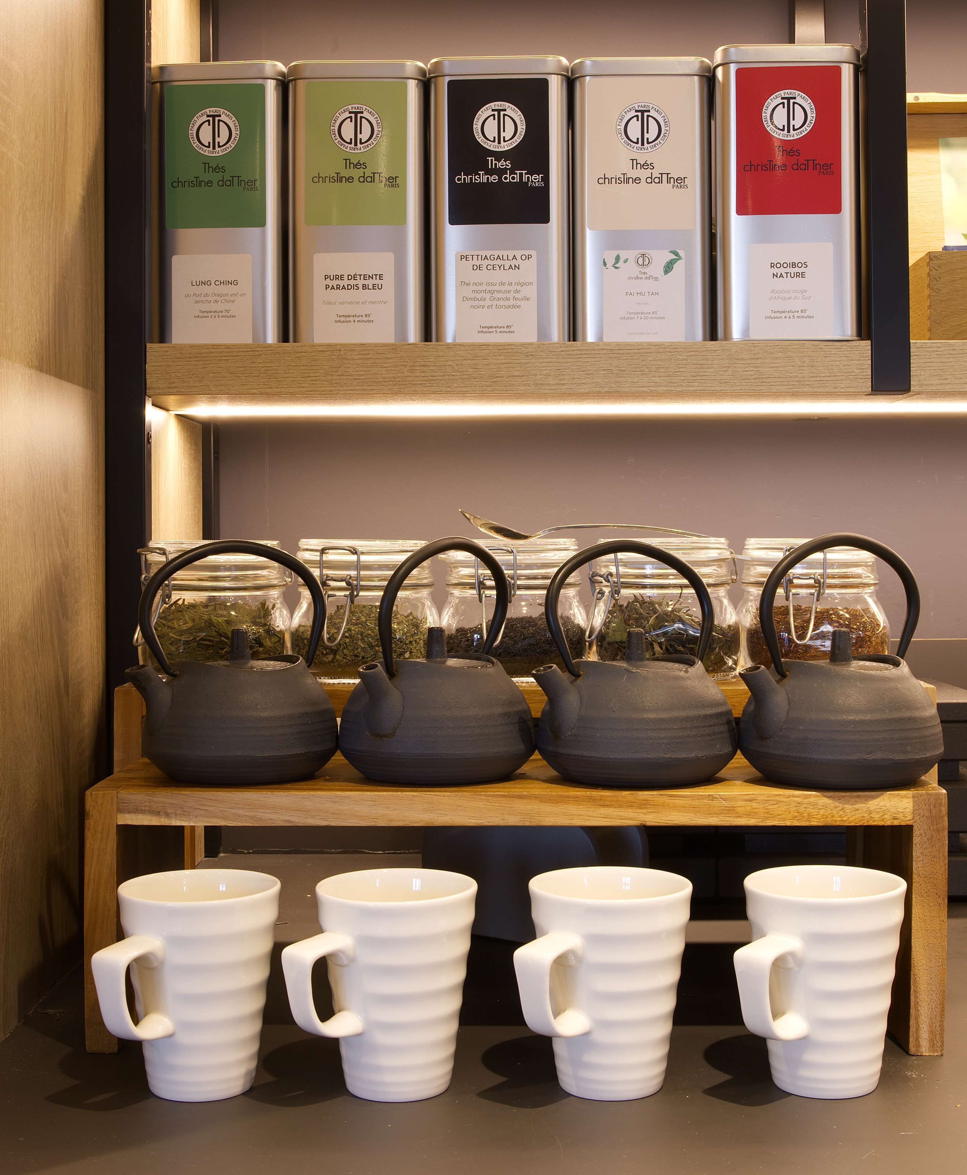 A display of tea tins and teapots on a shelf with white mugs in front.