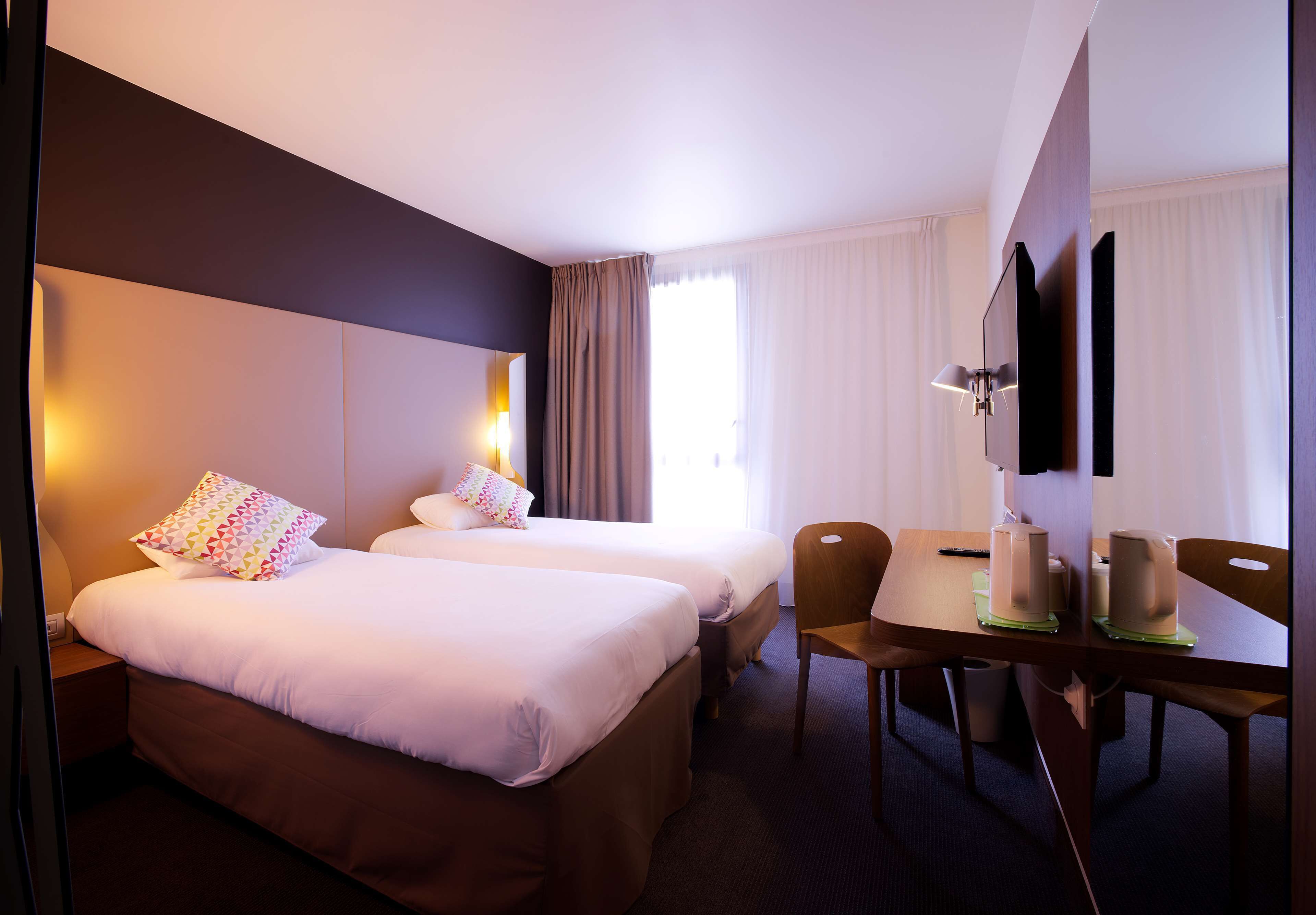 Une chambre d’hôtel avec deux lits, un bureau avec des chaises, un téléviseur à écran plat et une grande fenêtre avec des rideaux.