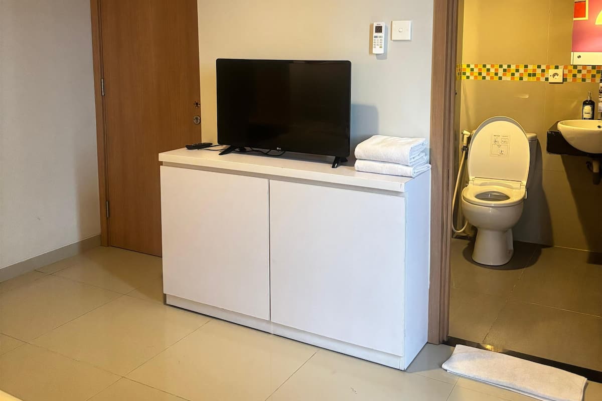 A small, clean room with a white cabinet, a television, a toilet, and a shower area.