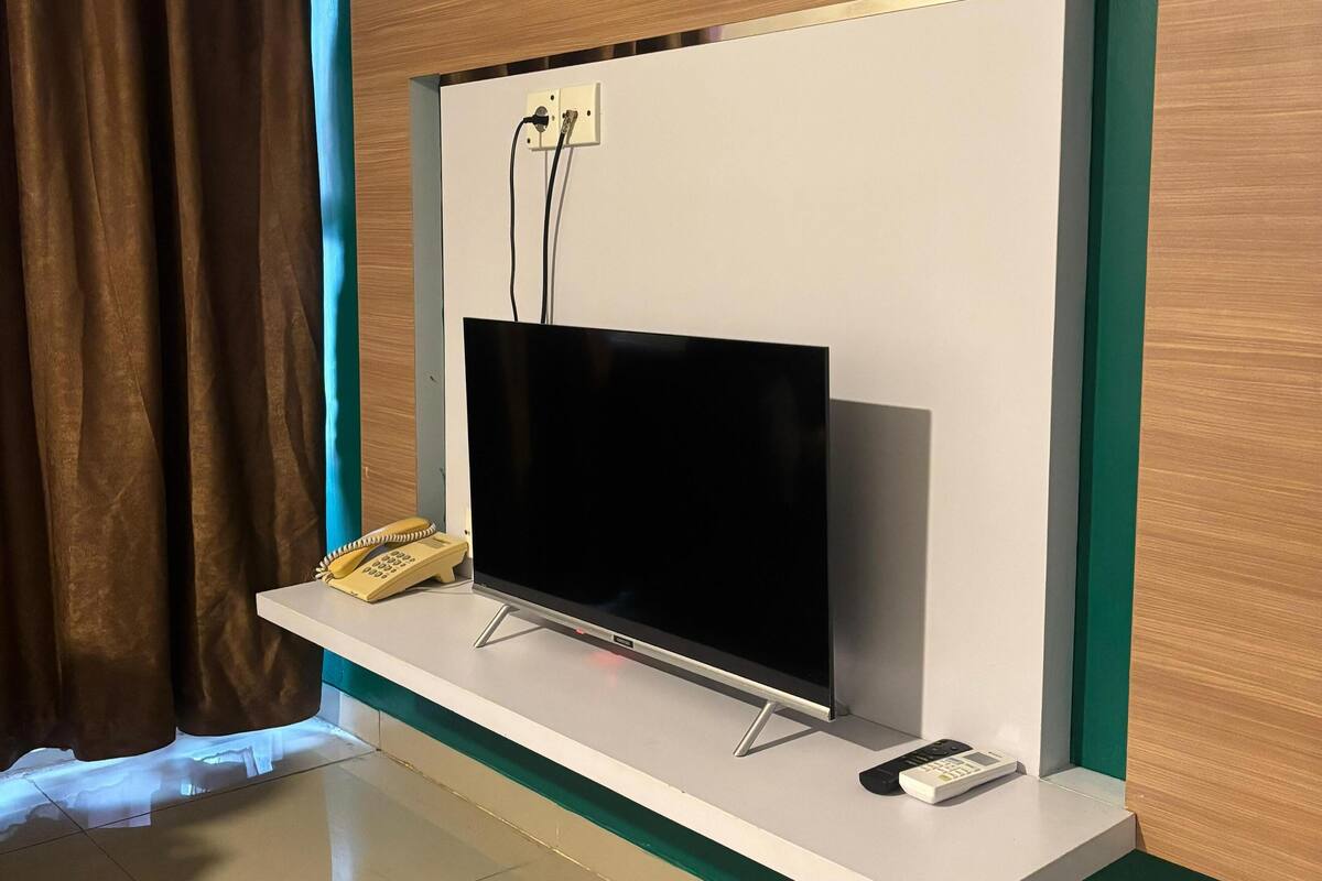 A modern living room with a flat-screen TV mounted on a white wall, a telephone, and a remote control on a shelf.