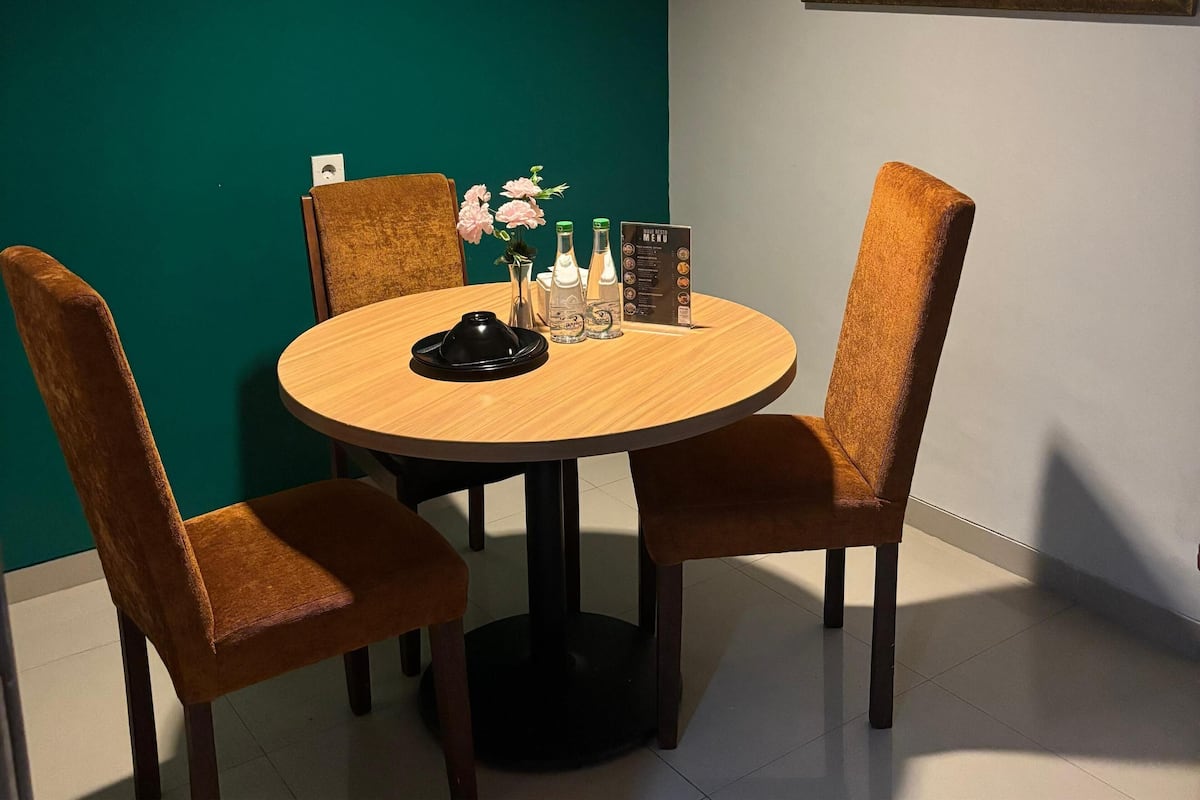 A dining area with a round table, four chairs, a menu, and a vase with flowers.