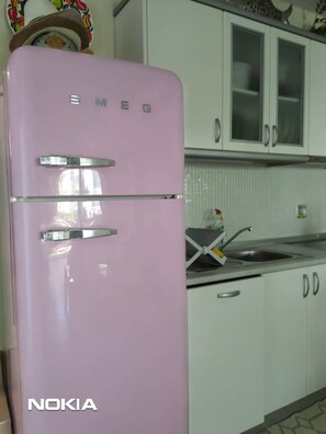 A pink refrigerator with the brand name 'NOKIA' and 'SMEG' on it, located in a kitchen with white cabinets and a sink.