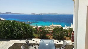 A patio with a view of the sea, a white building, and some greenery. - Cozy apartment for 2 near Ornos with sea and sunset view  (Ornos Mykonos)