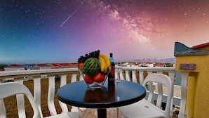 Une table avec un panier de fruits et une bouteille sur un balcon offrant une vue sur la Voie lactée.