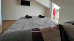 Une chambre avec un lit, un téléviseur fixé au mur et une fenêtre donnant sur l’extérieur.