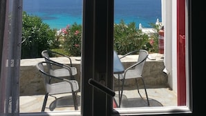 Une vue depuis une fenêtre donnant sur une zone côtière, avec un ciel dégagé, et sur laquelle on aperçoit une table et deux chaises sur un balcon.