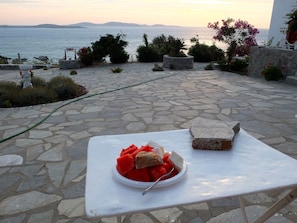 A stone-paved outdoor area with a table holding a bowl of fruit and a bottle.