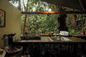 A kitchen with a gas stove, sink, and various utensils. There is a view of dense greenery outside. - Colina Secreta - Glamping and Villas (Cahuita)