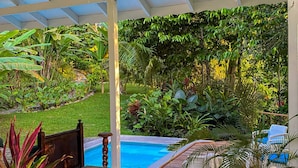 A covered outdoor area with a pool, wooden furniture, and lush greenery. - Colina Secreta - Glamping and Villas (Cahuita)