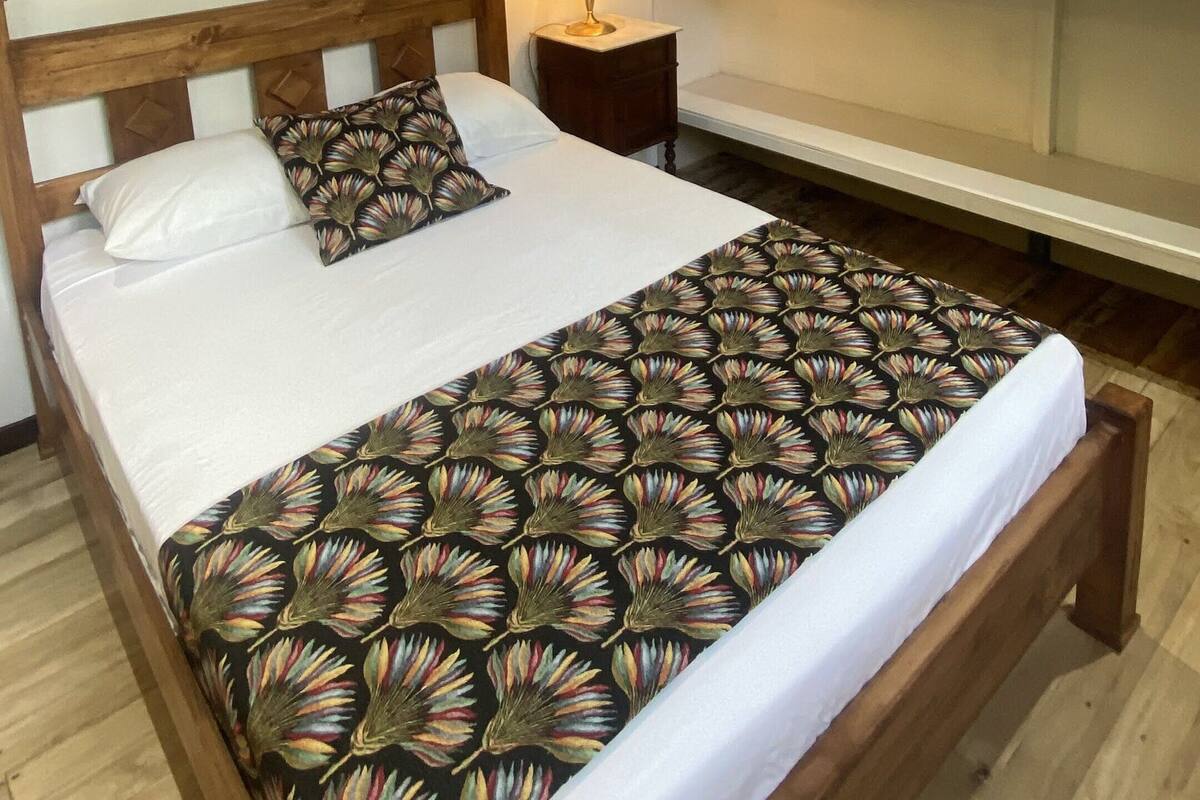 Ein ordentlich bezogenes Bett mit Blumendekoration, eine Nachttischlampe und ein Regal mit gefalteten Handtüchern.
