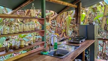 A rustic kitchen with a wooden countertop, shelves with jars, a sink, and a refrigerator.