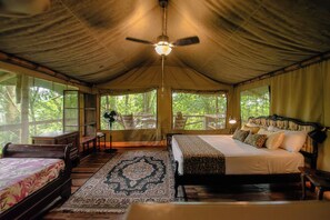 A tented accommodation with a bed, a desk, and a chair. - Colina Secreta - Glamping and Villas (Cahuita)