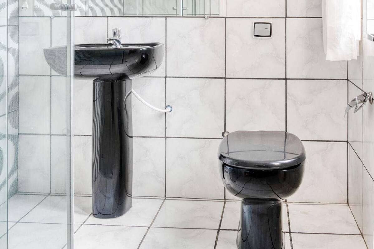 A bathroom with a glass shower enclosure, a black pedestal sink, and a black toilet.