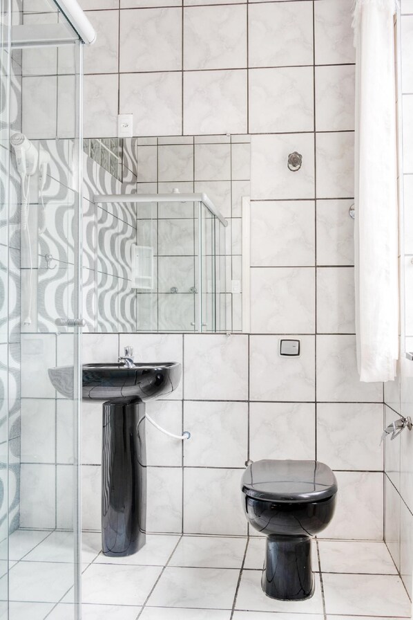 A bathroom with a glass shower enclosure, a black pedestal sink, and a black toilet.