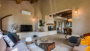 A spacious living room with a flat-screen TV, comfortable seating, a fireplace, and a staircase leading to an upper level.