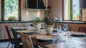 A dining area with a wooden table set for a meal, surrounded by chairs, with a view of greenery outside through large windows.