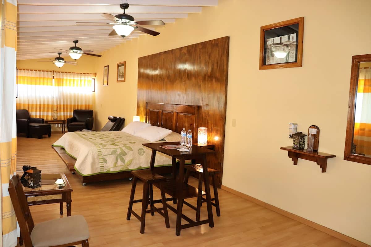 A hotel room with a bed, a desk, two chairs, a ceiling fan, and a wooden headboard.