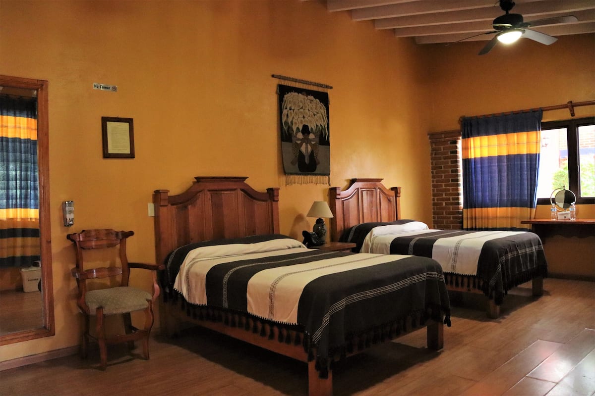 A hotel room with two wooden beds, a wooden chair, a ceiling fan, and a window with curtains.
