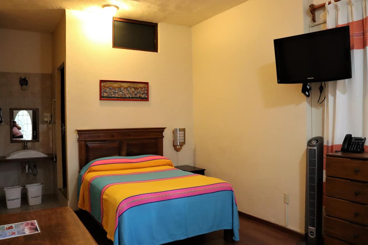 A hotel room with a bed, a television mounted on the wall, a wooden dresser, and a small window.