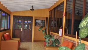 A spacious living area with a wooden floor, a brown sofa, a red armchair, and a large potted plant. - Hotel Zaragoza Tepoztlan (Tepoztlán)