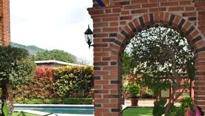A brick archway leading to a pool area with a well-maintained lawn and potted plants. - Hotel Zaragoza Tepoztlan (Tepoztlán)