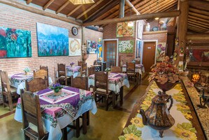 Un comedor rústico con paredes de ladrillo, mesas y sillas de madera, decorado con motivos florales y obras de arte.