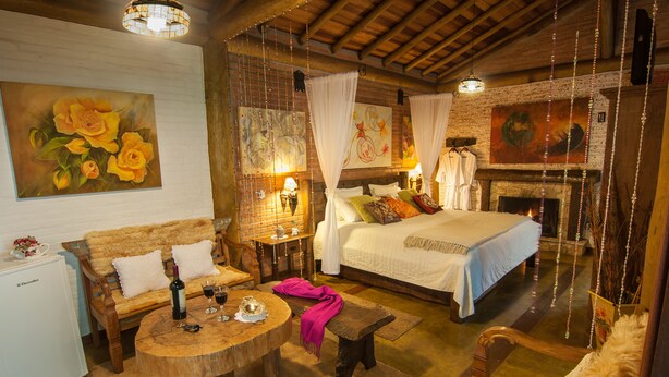 A cozy room with a bed, a wooden table, and a fireplace. - Pousada Alto da Neblina (Camanducaia)
