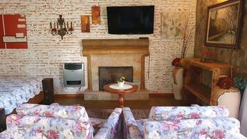 Una sala de estar acogedora con chimenea, sofás de estampado floral, un televisor montado en la pared y un cuadro enmarcado.