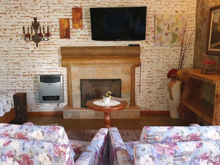 Una sala de estar acogedora con chimenea, sofás de estampado floral, un televisor montado en la pared y un cuadro enmarcado.
