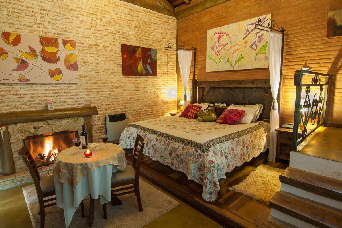 A cozy room with a fireplace, a bed with floral bedding, and artwork on the walls.