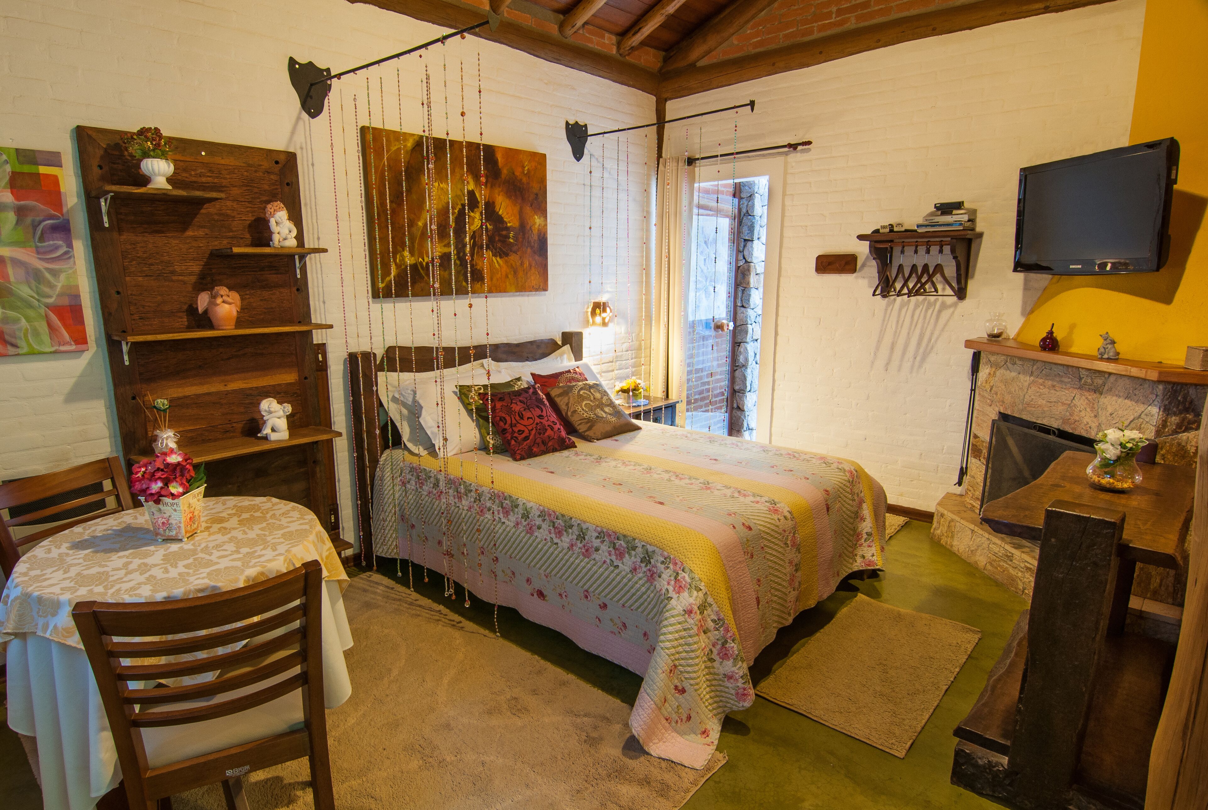 Een knus slaapkamer met een bed, een houten stoel, een klein tafeltje, een televisie en een open haard.