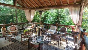 A covered outdoor seating area with wicker furniture, a table, and a hanging light fixture. - Pousada Alto da Neblina (Camanducaia)