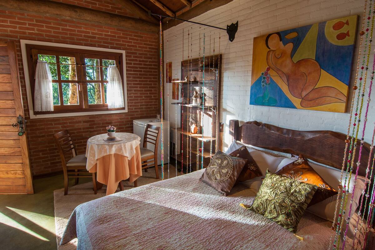 A rustic room with a bed, a dining table, and a window with curtains.