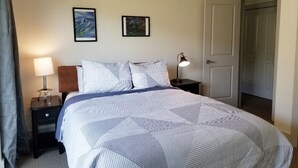 A neatly made bed with a striped bedspread and pillows, a bedside lamp, and two framed pictures on the wall. - Big Sky Haven, Quiet and Centrally Located for Skiing, Fishing, Golfing 
 (Big Sky)