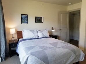 Una cama bien hecha con cubrecama a rayas y almohadas, una lámpara de noche y dos cuadros en la pared.