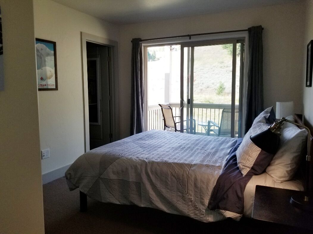 Ein Schlafzimmer mit Bett, Stuhl, Tisch und Blick ins Freie durch eine Schiebetür.
