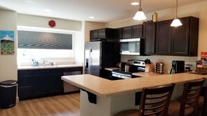 A modern kitchen with dark cabinets, a central island with bar stools, stainless steel appliances, and pendant lighting. - Big Sky Haven, Quiet and Centrally Located for Skiing, Fishing, Golfing 
 (Big Sky)