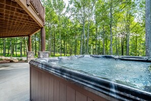 A hot tub in a wooded area with a wooden deck and stone pillars. - Away in the Mountains (McHenry)