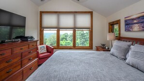 A bedroom with a large bed, a TV on a wooden dresser, a window with blinds, a ceiling fan, and a painting on the wall. - Eagle's Rest (McHenry)