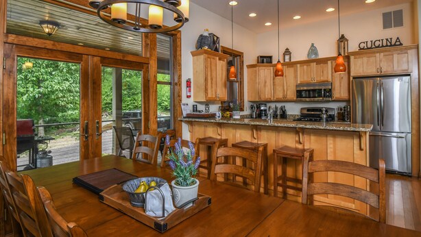 A spacious kitchen with wooden cabinets, a stainless steel refrigerator, and a dining area with a wooden table and chairs. - Eagle's Rest (McHenry)