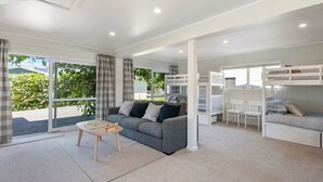 A modern, well-lit living room with a grey sofa, a wooden coffee table, and a white desk. There is a bunk bed with a white headboard and a white chair.