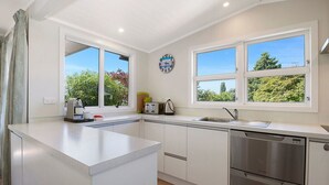 A modern kitchen with white cabinetry, a built-in dishwasher, and large windows offering views of greenery.