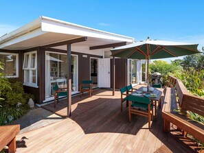 Een houten terras met buitenmeubilair, een overdekte patio en uitzicht op de omliggende tuin.