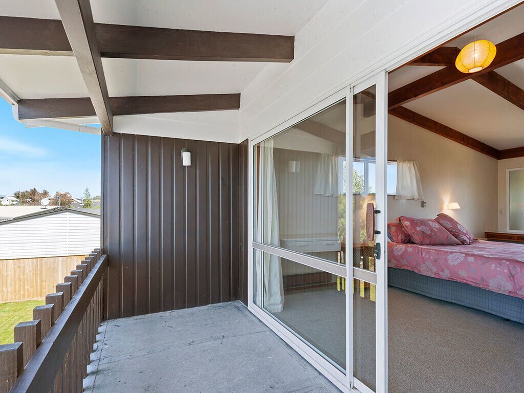 A balcony with a view of a house, a bedroom with a bed and a nightstand, and a sliding glass door.