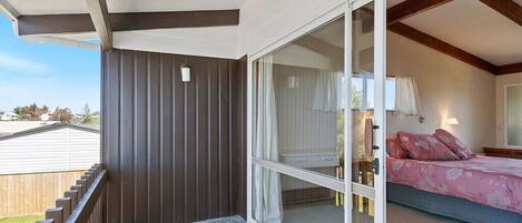 A balcony with a view of a house, a bedroom with a bed and a nightstand, and a sliding glass door.